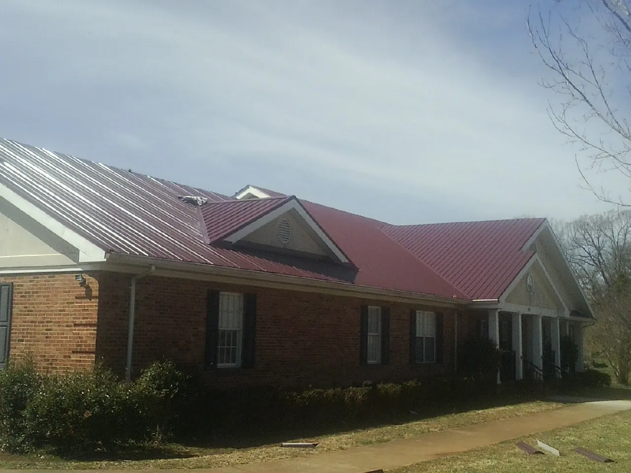 Red metal roof with gabled entries on a long brick building, from a Hail Damage Roof Repair job in Marianna