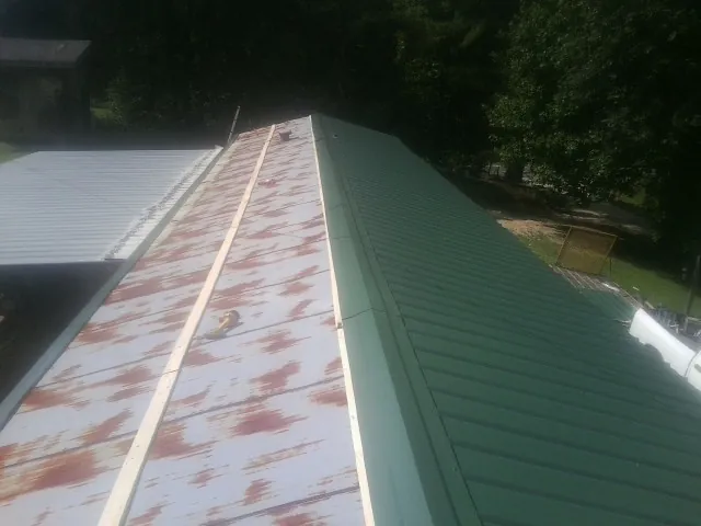 Old rusted panels beside newly installed green metal roofing — Wind Damage Roof Repair by Roofing Brothers in Marianna